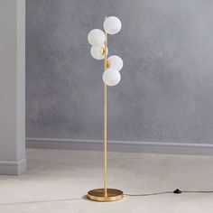 a floor lamp with four white glass balls on the base and a gold plated metal stand