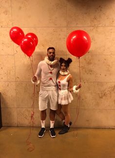 a man and woman dressed up as clowns holding red balloons in front of a wall