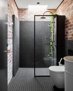 a modern bathroom with brick walls and black tiles on the shower wall, along with a white toilet