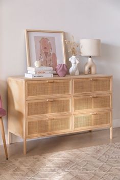 a wicker dresser with books, vases and pictures on it in front of a white wall