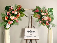 three floral arrangements on easel with welcome to our engagement party sign in front of them