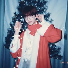 a young man wearing glasses standing in front of a christmas tree with lights on it