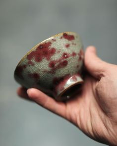 a hand holding a small cup with red splatters on it's surface