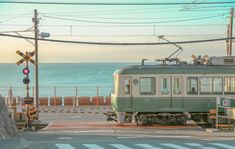 a green train traveling down tracks next to the ocean with power lines above it and an orange traffic light