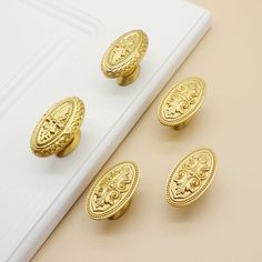 four gold knobs on a white surface next to a pair of scissors and a napkin