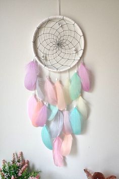 a white dream catcher with pastel feathers hanging from it's side on a wall