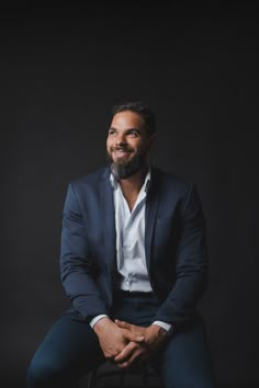 a man sitting on top of a chair in front of a black background wearing a suit