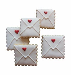 four decorated cookies in the shape of envelopes with red hearts on them, all lined up and ready to be eaten