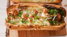 two pieces of bread with meat and cheese on them sitting on a wooden cutting board