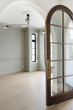 an empty room with wooden floors and arched doorway leading to another room that has large windows