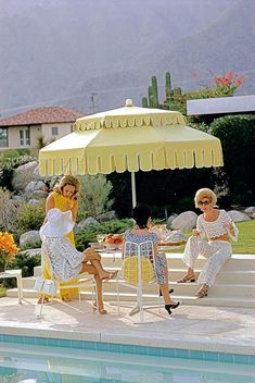 two women sitting under an umbrella next to a pool