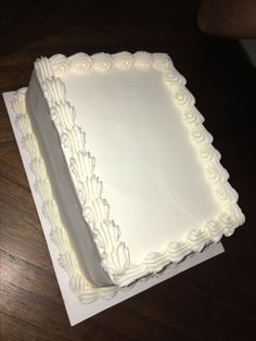 a square white cake sitting on top of a wooden table next to a person's hand