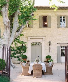 an outdoor dining area with wicker chairs and table in front of a stone building