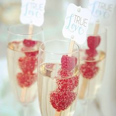 three wine glasses filled with raspberries on top of a white table topped with strawberries