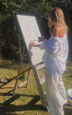 a woman standing in front of a white easel painting on the side of a field