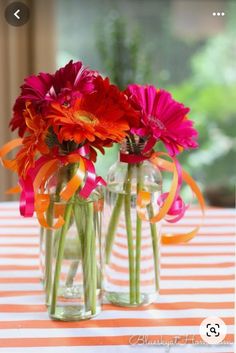 two vases filled with colorful flowers on top of a striped tablecloth covered table