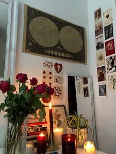 candles and flowers are on a table in front of a mirror with pictures above it