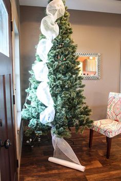 a decorated christmas tree in the corner of a room with a chair and mirror on the wall