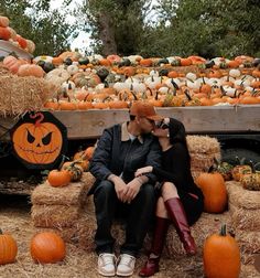 a man and woman sitting on hay with pumpkins in the background