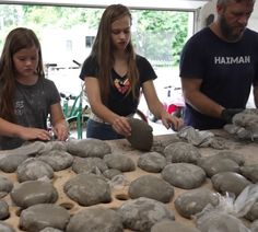 two girls and an older man are making stoneware at a table with other people looking on