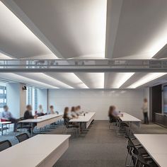 people are sitting at long tables in an office setting with large screens on the wall