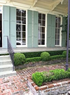 a woman standing in the doorway of a house with blue shutters and green plants