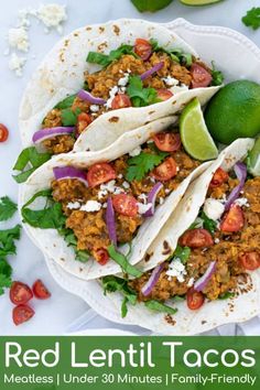 three tacos on a plate with limes and tomatoes