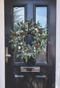 a wreath is hanging on the front door with pine cones and greenery around it