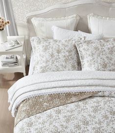 a bed with white and brown comforters in a bedroom next to a nightstand on a wooden floor