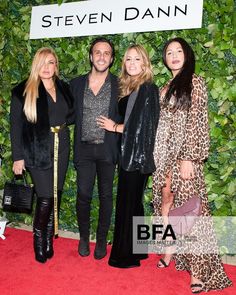 three women and one man standing next to each other in front of a green wall