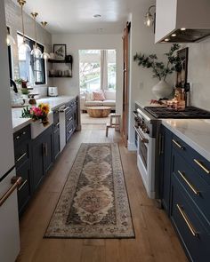 a long narrow kitchen with blue cabinets and white counters, along with a rug on the floor