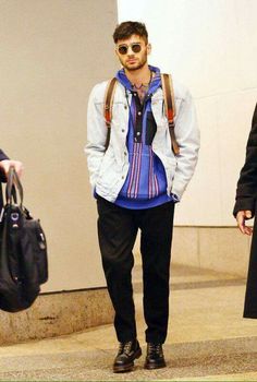 a young man wearing sunglasses and a backpack walks through an airport with his hand in his pocket