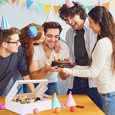 a group of young people standing around a table with a cake in front of them