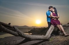 a man and woman embracing each other while sitting on a tree branch in front of the sun