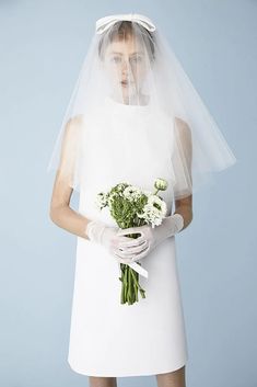 a woman in a white dress holding a bouquet of flowers and wearing a veil over her head