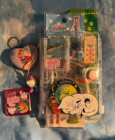 an assortment of items in a plastic case on a blue cloth covered surface with tags and keychains