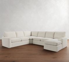 a white sectional couch sitting on top of a hard wood floor next to a wall