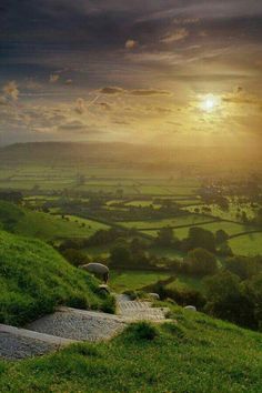 the sun is setting over green hills and fields with steps leading up to them in the foreground