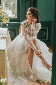 a woman in a wedding dress sitting at a table with flowers on it and holding her hand up to her face