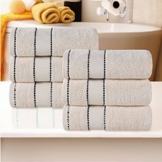 four white towels stacked on top of each other in front of a bathtub and sink