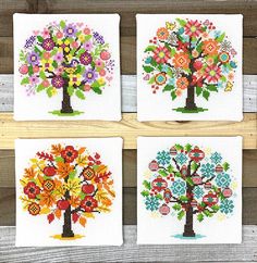 four cross stitch coasters with colorful tree designs on them, hanging on a wooden fence