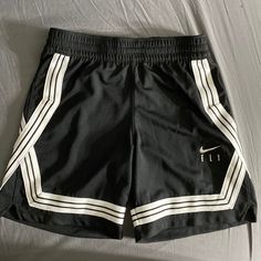 1. Pair Of Shorts 2. Hanging On A Wall 3. Black Color 4. Nike Brand 5. White Stripes On Sides 6. Word "Fly" Written On Right Leg 7. Nike Swoosh Above "Fly" 8. Made For Basketball 9. Athletic Style 10. Elastic Waistband 11. Drawstring For Adjustment 12. Lightweight Material 13. Breathable Fabric 14. Knee-Length 15. Loose Fit 16. Double-Stitched Seams 17. Moisture-Wicking Technology 18. Suitable For Sports 19. Trendy Design 20. Comfortable Wear Cheap Nike Black Athletic Shorts, Affordable Black Nike Athletic Shorts, Basketball Shorts Women Outfit, Womens Basketball Shorts, Western Fits, Nike Basketball Shorts, Athletic Clothes, Basketball Clothes, Nike Brand