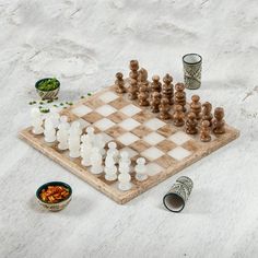 a chess board with several pieces on it and two small cups next to the board