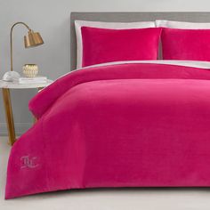 a bright pink comforter with white trim on a bed in a gray room next to a lamp