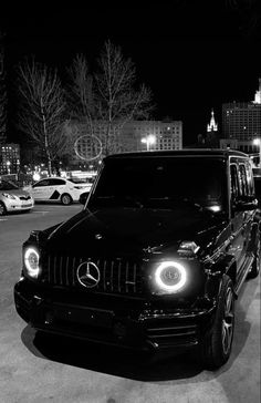 a black mercedes g class parked in a parking lot at night with the lights on