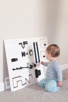 a baby sitting on the floor next to a white board with black handles and knobs