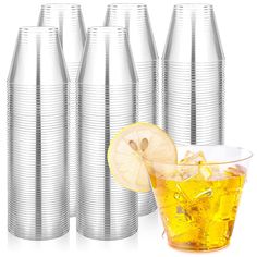 a glass filled with lemonade next to several stacks of silver cups and a half - eaten lemon