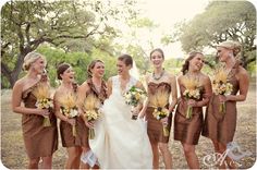 a group of women standing next to each other in front of trees and grass holding bouquets