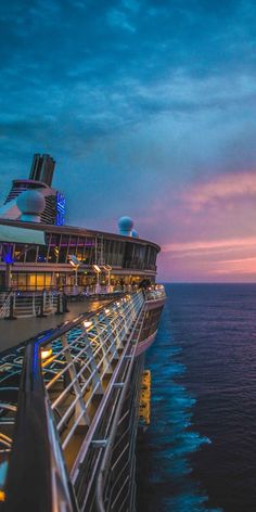 the deck of a cruise ship at dusk with its lights on and water in the foreground