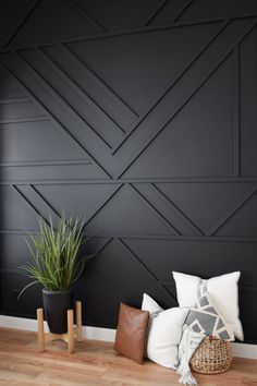 a black wall with some pillows and plants on the floor in front of it, along with two wooden stools